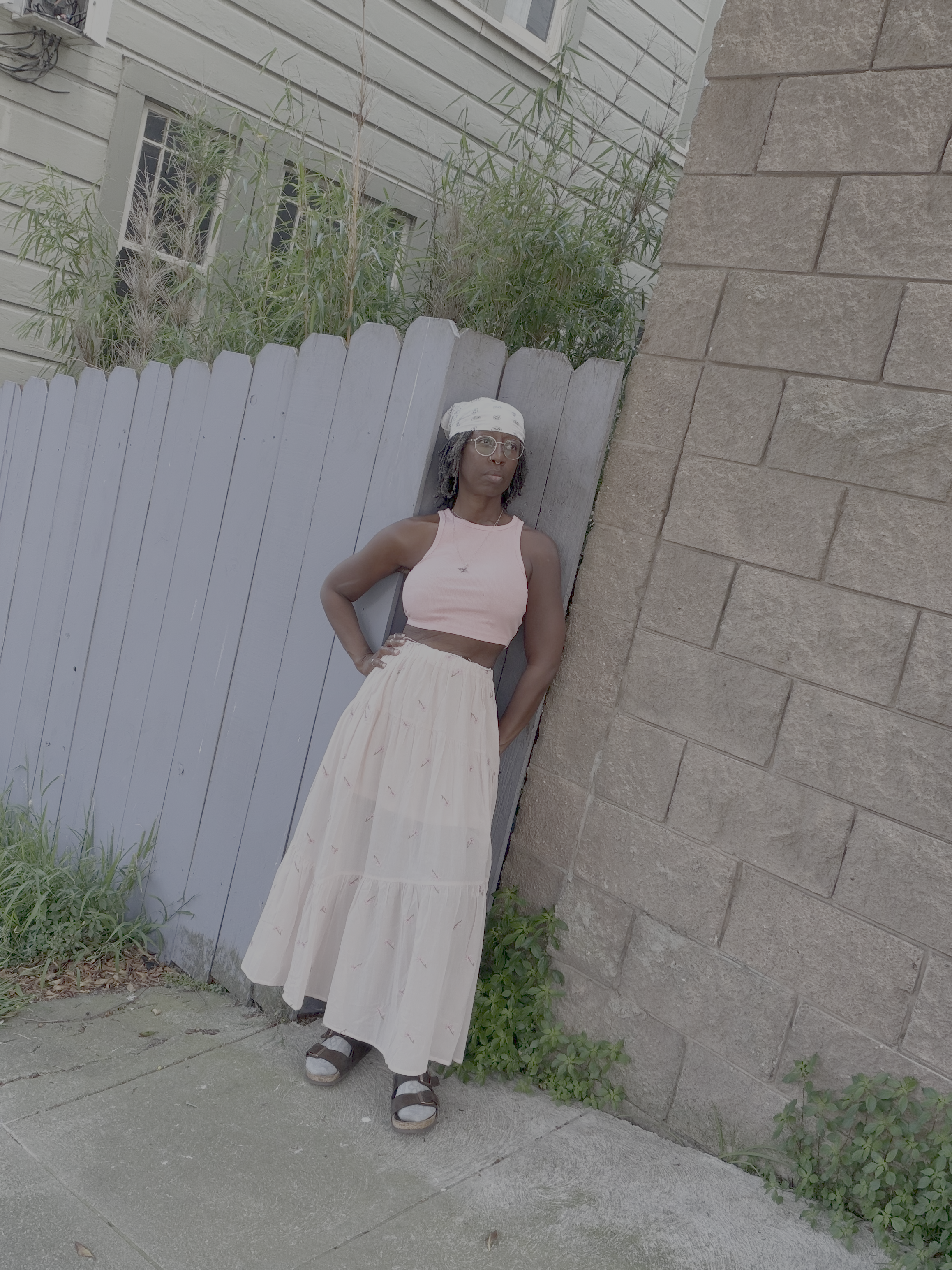 Woman in a pink crop top and pink flowy midi embroidery floral skirt leaning against a stone wall outdoors"