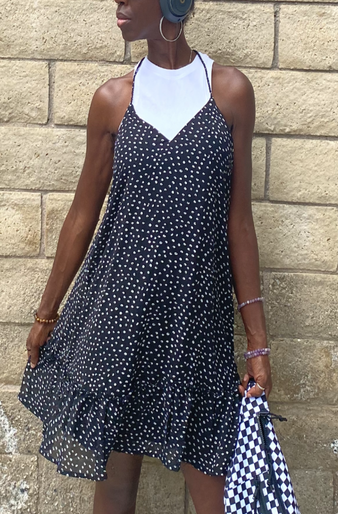 Woman wearing a black dotted cami dress with a white high-neck undershirt, styled for an everyday look against a brick wall.