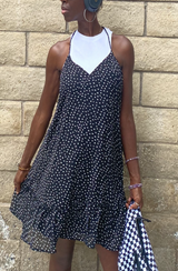 Woman wearing a black dotted cami dress with a white high-neck undershirt, styled for an everyday look against a brick wall.