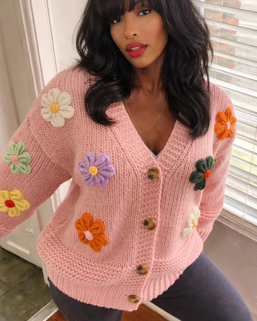 Woman wearing a pink cardigan with floral patches indoors.