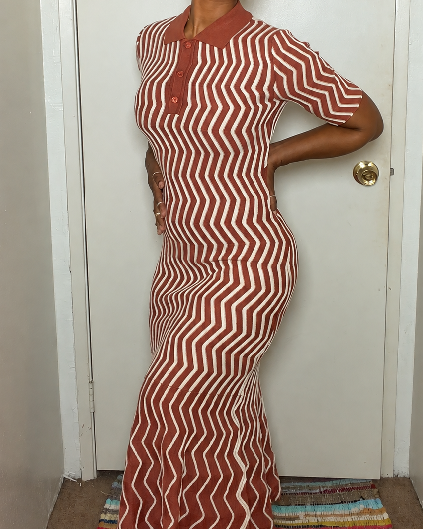A woman wearing a short-sleeve polo-style maxi dress with a rust-orange and cream zigzag stripe pattern, standing in front of a white door.