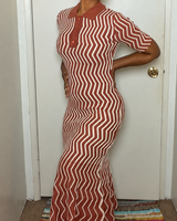 A woman wearing a short-sleeve polo-style maxi dress with a rust-orange and cream zigzag stripe pattern, standing in front of a white door.