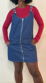 Women’s zip-front denim overall mini dress with adjustable straps over red long-sleeve top — fall casual outfit idea.