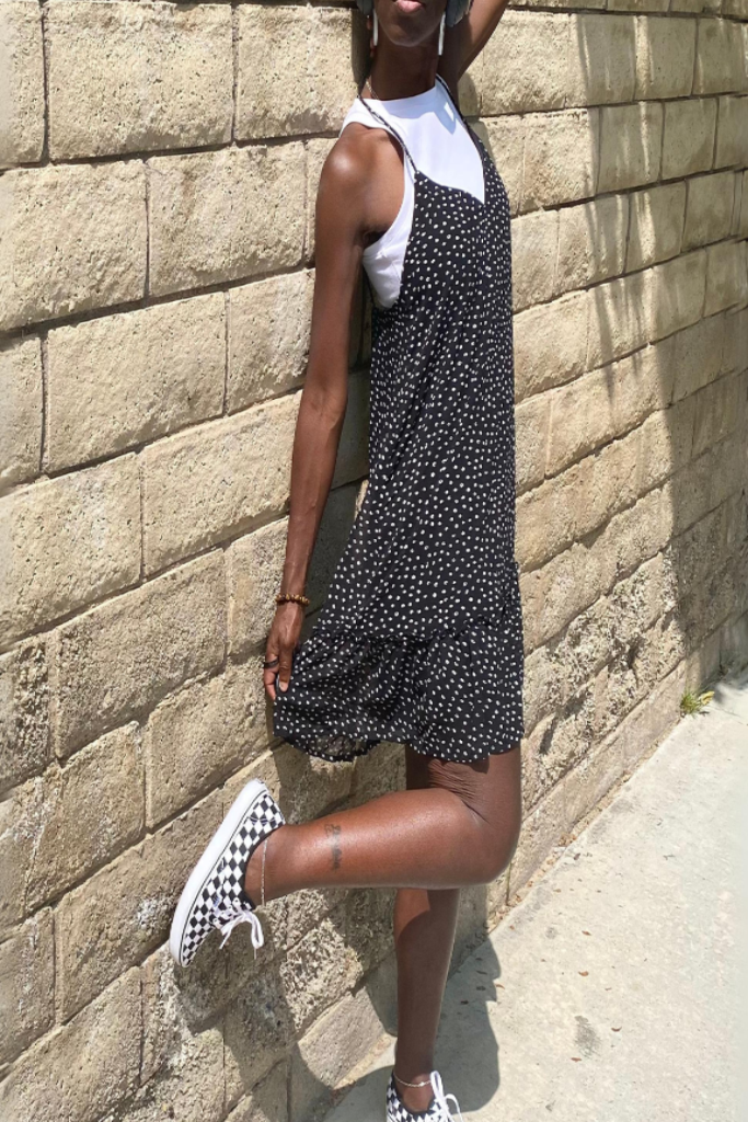 model wear white cropped top underneath a flowy black mini cami dress with irregular dot pattern and twisted spaghetti straps – stylish and flirty summer staple. model is wearing classic VAN checked shoes