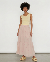 Woman wearing a blush pink floral embroidered tiered midi skirt with a light yellow sleeveless top.