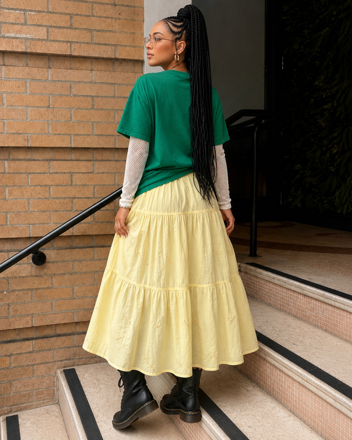 Back view of a buttery yellow floral embroidered tiered midi skirt styled with an oversized green graphic tee and black lace-up boots.