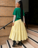 Back view of a buttery yellow floral embroidered tiered midi skirt styled with an oversized green graphic tee and black lace-up boots.