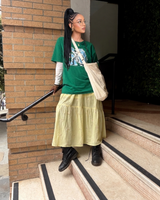 Woman wearing a buttery yellow floral embroidered tiered midi skirt styled with an oversized green graphic tee, cream crossbody bag, and black lace-up boots.