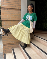 Woman wearing a buttery yellow floral embroidered tiered midi skirt styled with an oversized green graphic tee and black boots.
