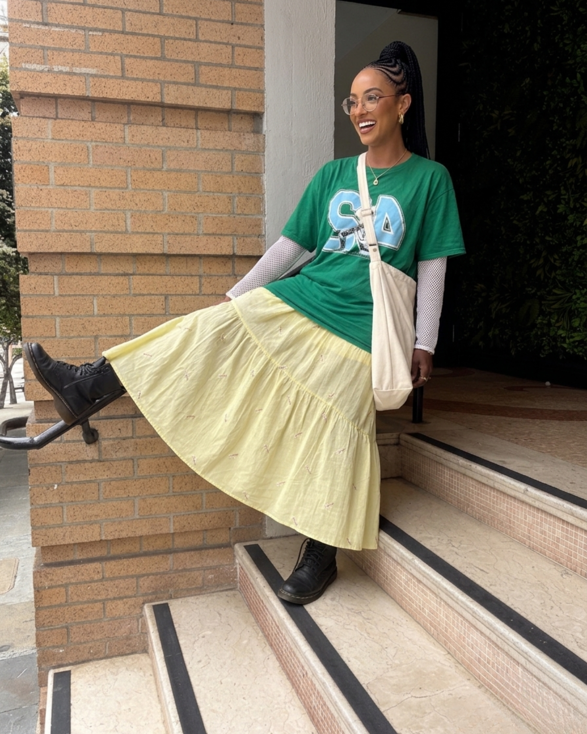 Woman wearing a buttery yellow floral embroidered tiered midi skirt styled with an oversized green graphic tee and black boots.