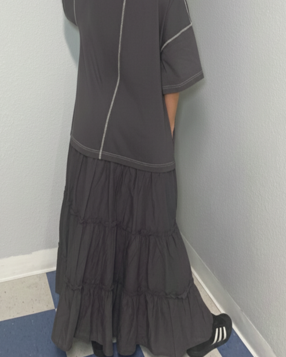 Woman wearing a dark gray dress with a white trim, standing against a plain wall.