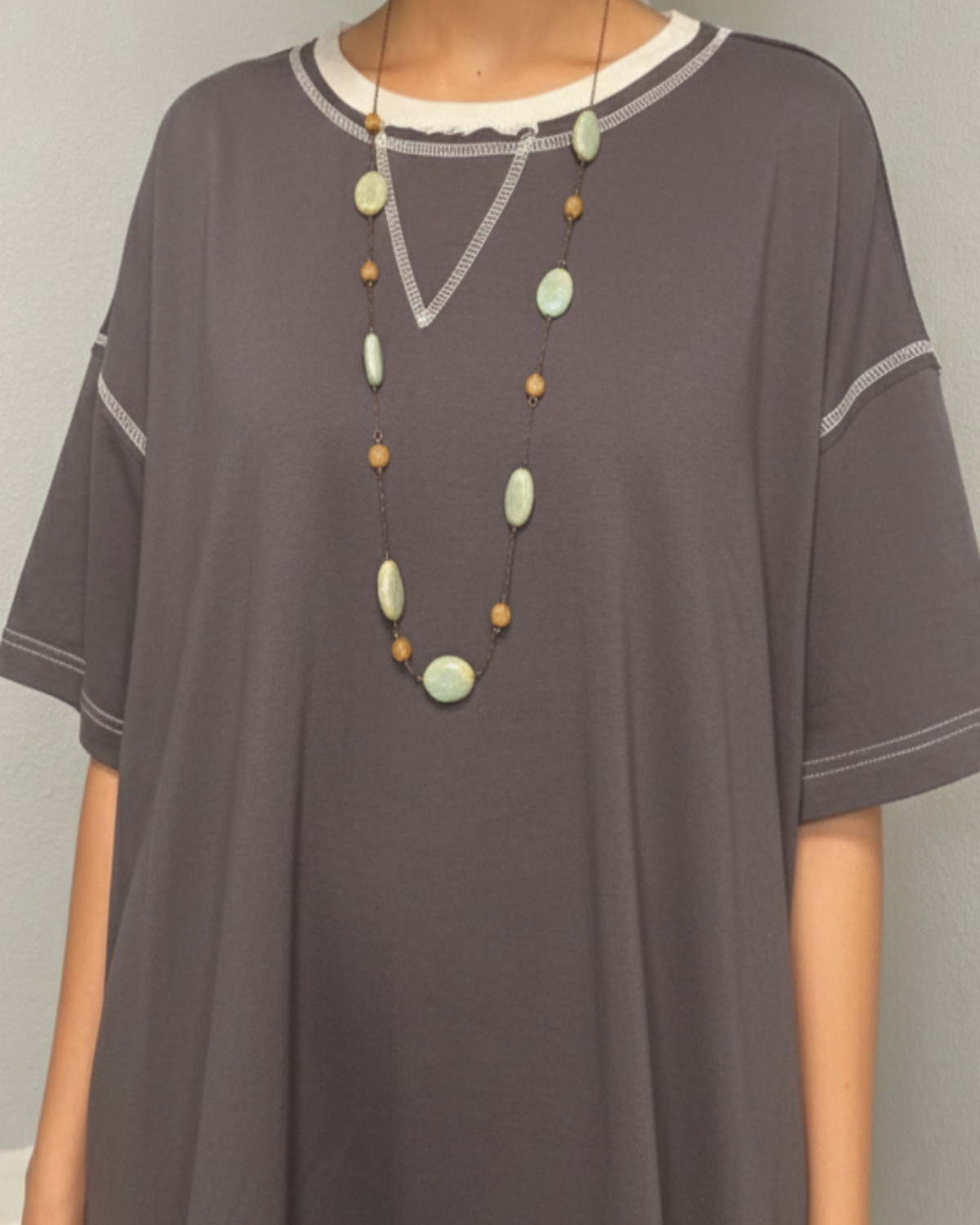 Woman wearing a gray tunic with a necklace against a plain background