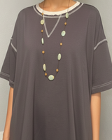 Woman wearing a gray tunic with a necklace against a plain background