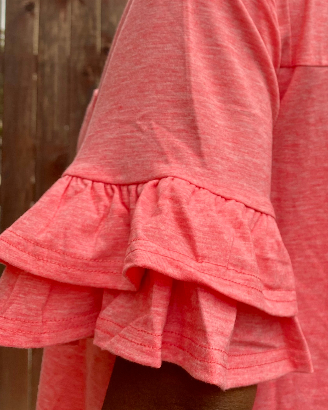 Close-up of the layered ruffle sleeve detail on a coral casual dress.