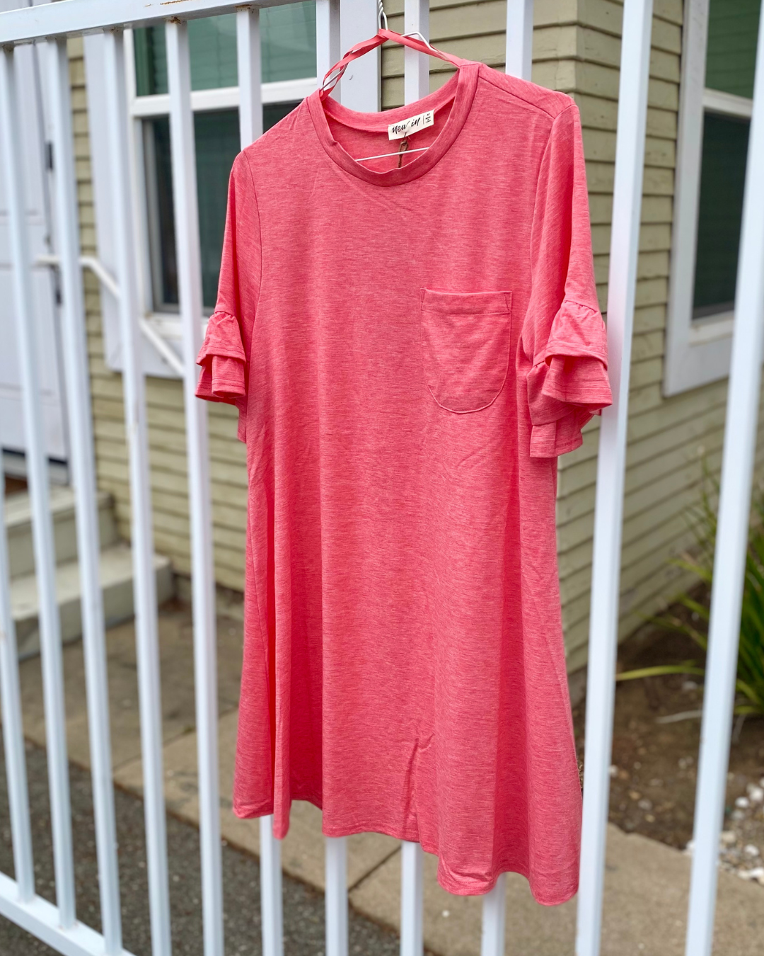 Coral ruffle sleeve t-shirt dress with a chest pocket hanging on a hanger, shown in a casual boutique product photo.