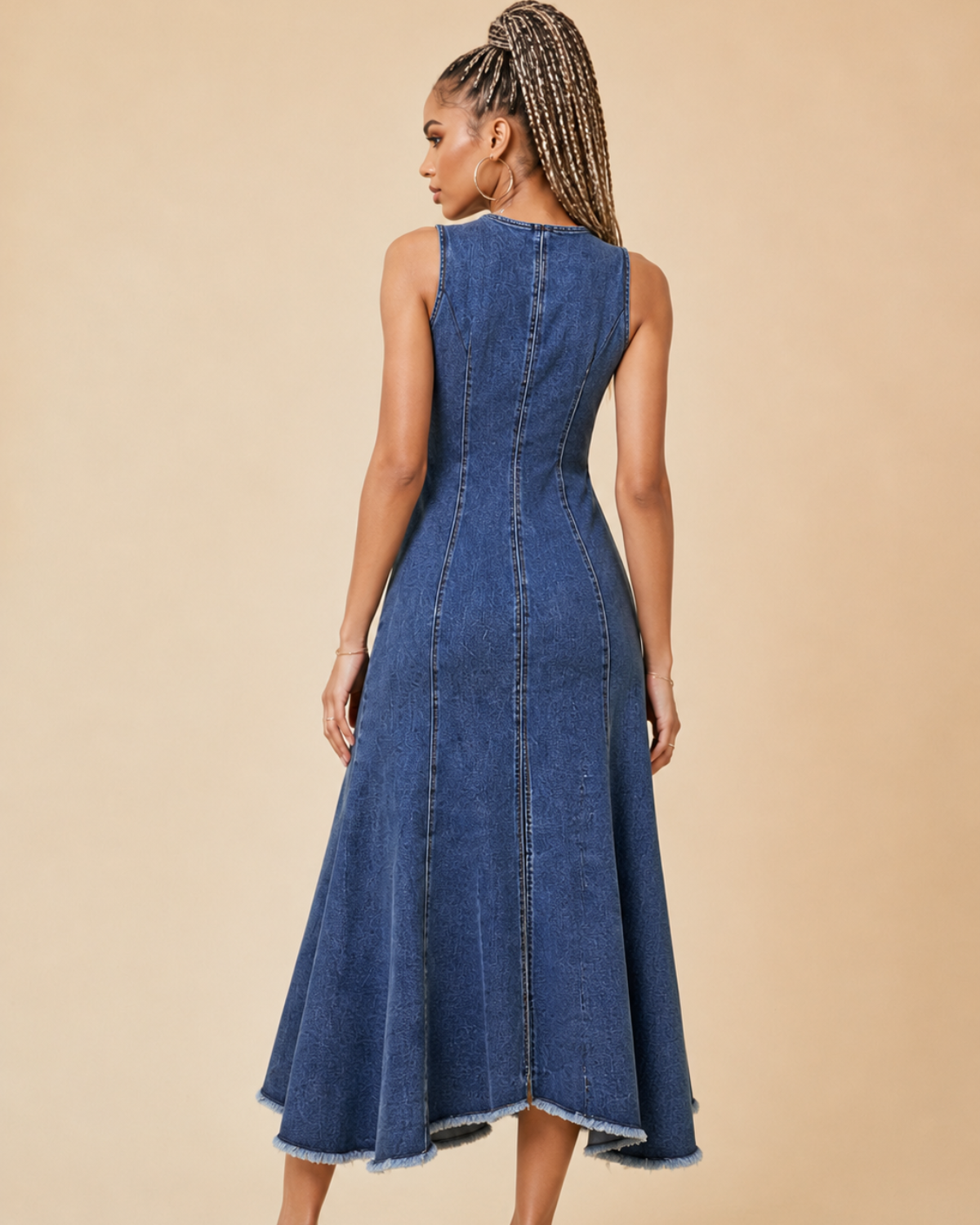 Back view of a women's dark rinse denim midi dress with front zipper detail, panel seams, and frayed hem, shown on a model against a beige studio background.