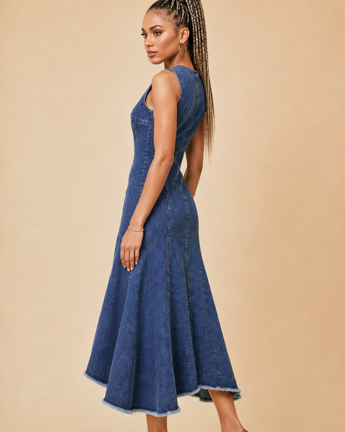 Side profile view of a women's dark rinse denim midi dress with front zipper closure, fitted bodice, panel seam details, and frayed hem, styled with tan heels against a beige studio background.