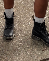 Person wearing black boots and white socks on a concrete surface