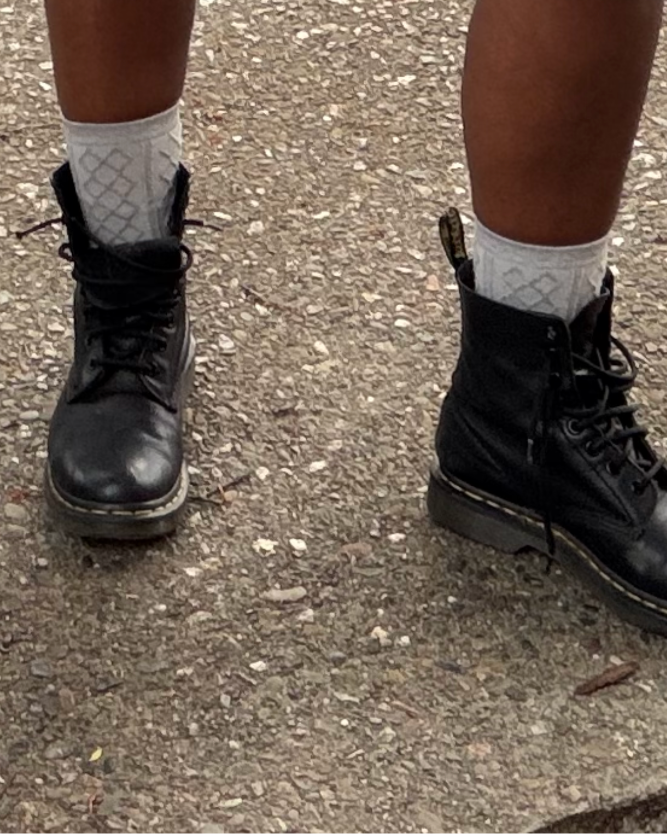 Person wearing black boots and white socks on a concrete surface
