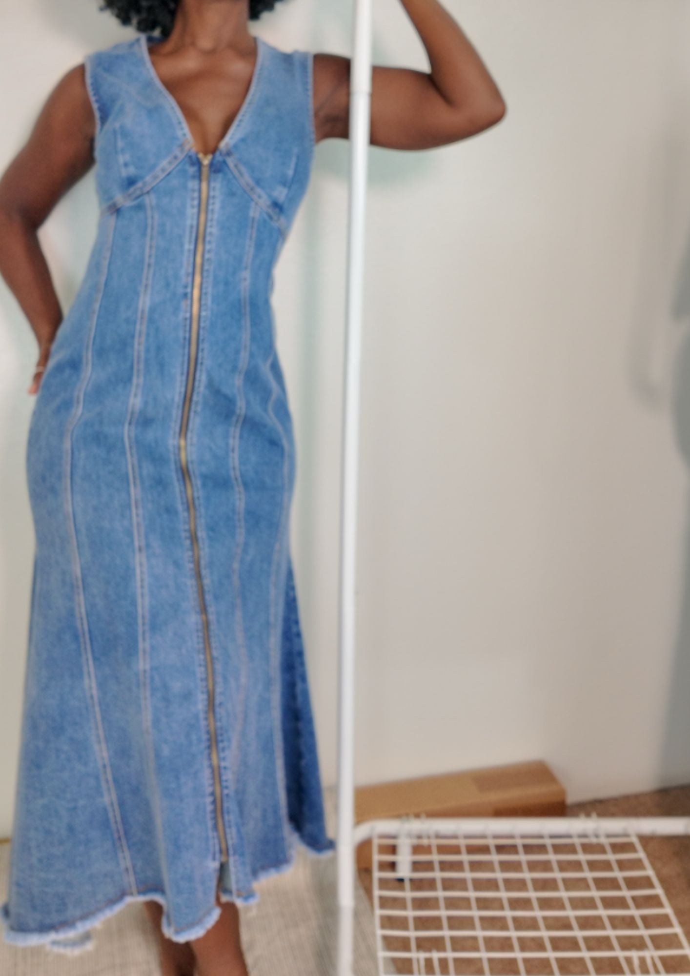 Close-up front of long denim zip-front dress in classic denim blue showing V-neck, paneled seams, and raw hem.
