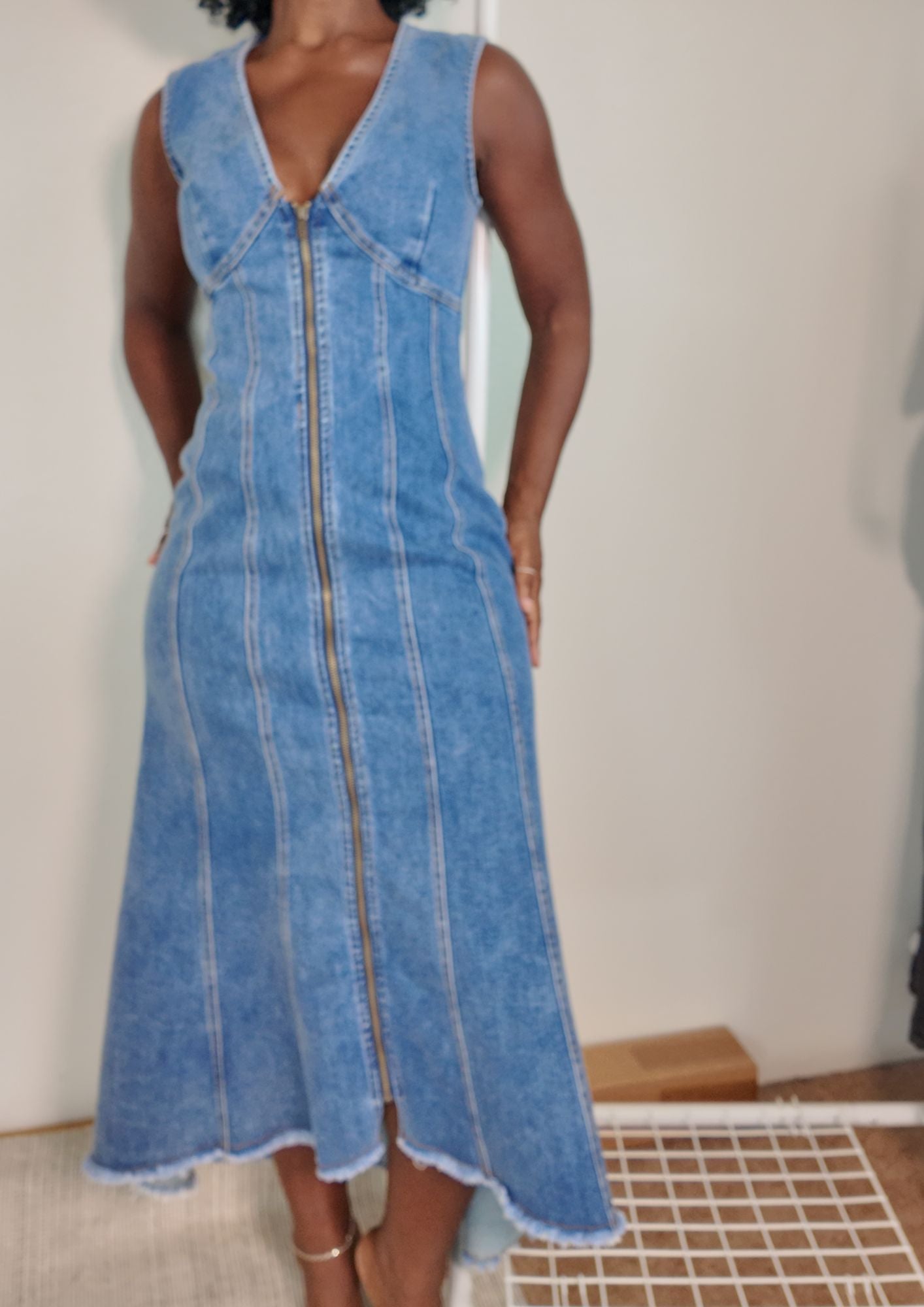 Model wearing long zip-front denim dress with paneled seams and raw hem.