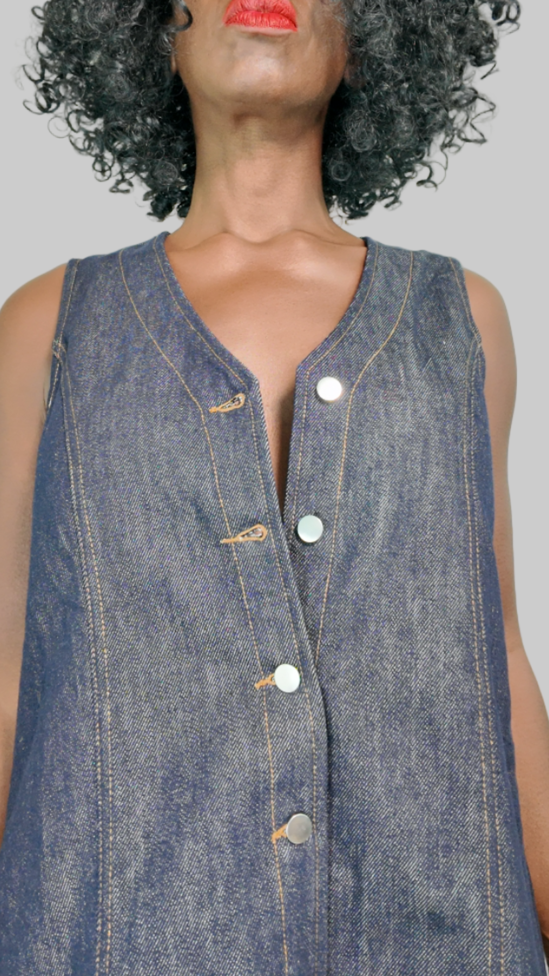 Close-up of short button-front denim dress in dark indigo showing V-neck, silver buttons, and contrast stitching